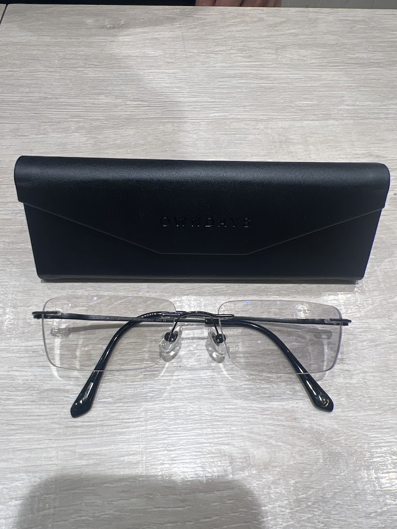 A pair of sleek rimless eyeglasses and a black OWNDAYS case on a light wooden surface.