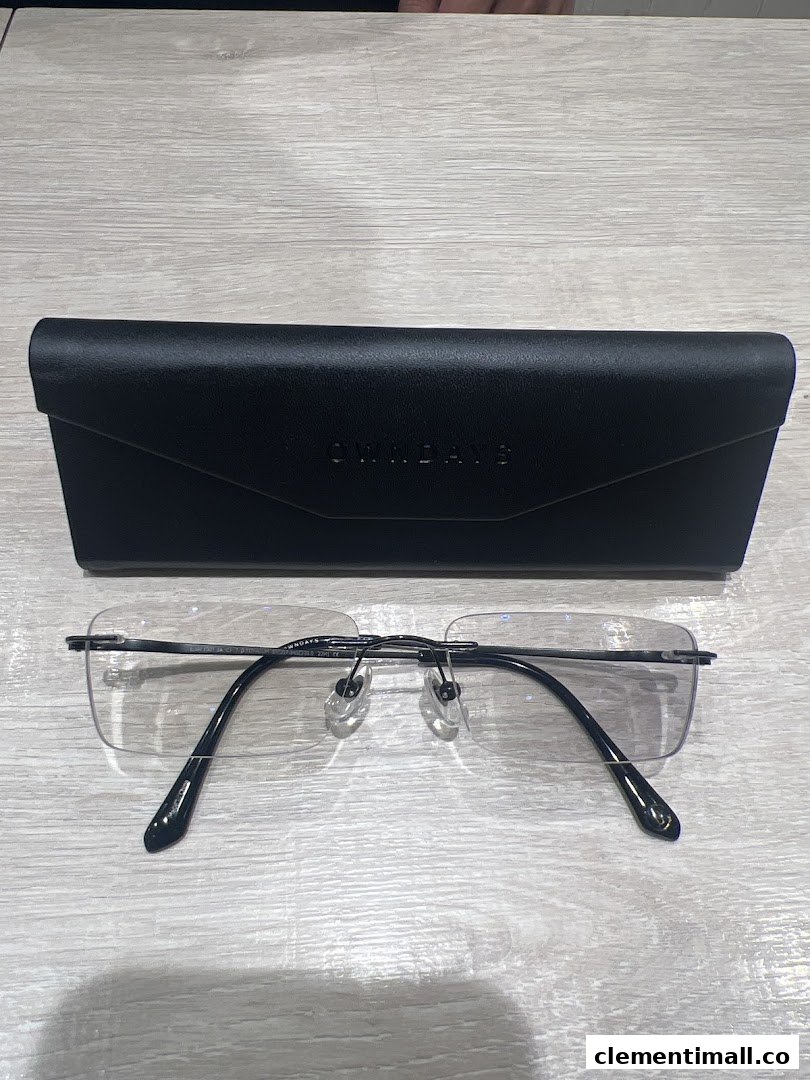 A pair of sleek rimless eyeglasses and a black OWNDAYS case on a light wooden surface.