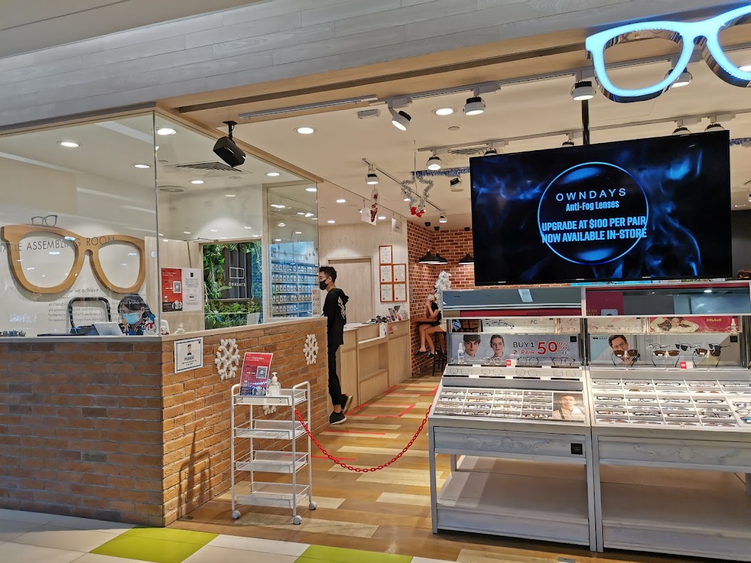 Interior view of OWNDAYS eyewear shop, showcasing product displays, a service counter, and promotional screens.