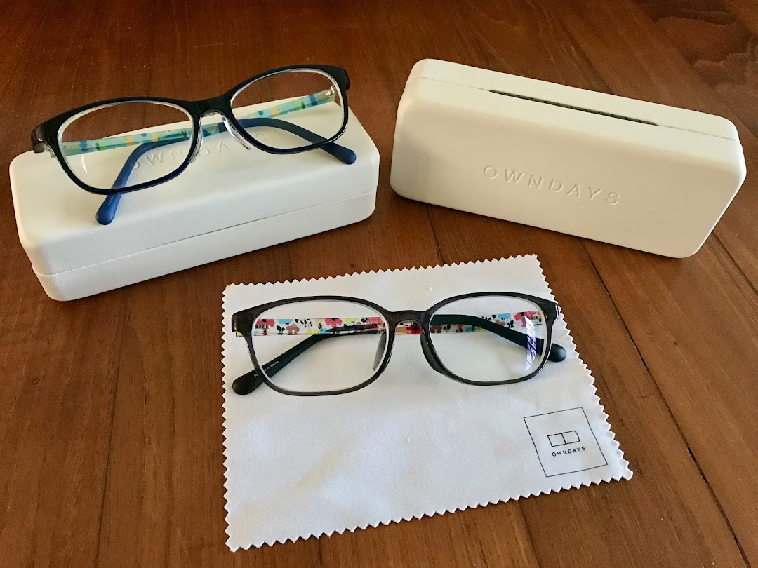 Two pairs of stylish OWNDAYS eyeglasses with cases and a cleaning cloth on a wooden surface.