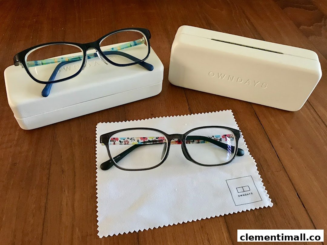 Two pairs of stylish OWNDAYS eyeglasses with cases and a cleaning cloth on a wooden surface.