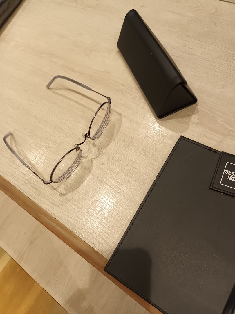 A pair of stylish round eyeglasses and a case on a light wooden surface.