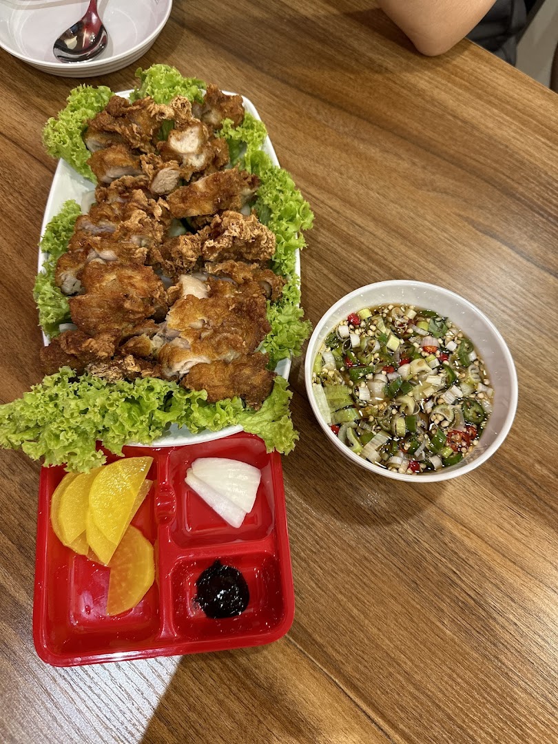 A plate of crispy fried chicken with fresh lettuce, a spicy dipping sauce, and pickled sides on a wooden table.