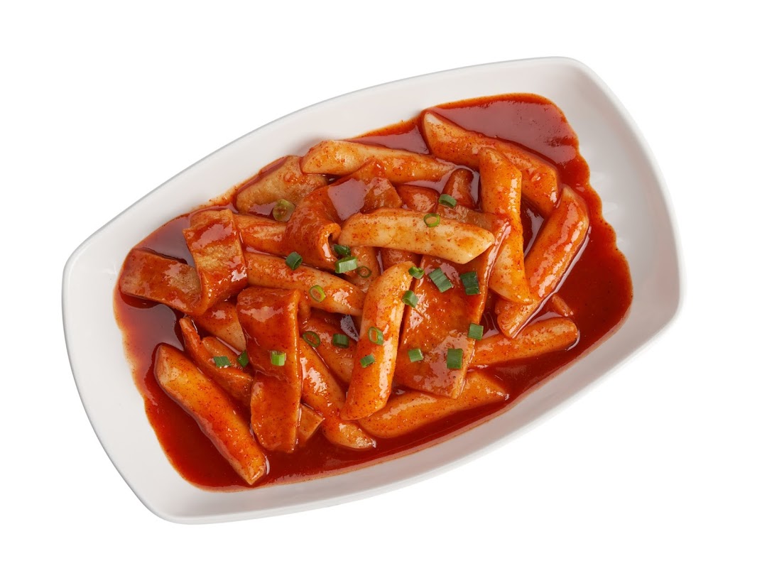 A white dish filled with spicy red Tteokbokki (Korean rice cakes) and fish cakes, garnished with green onions.