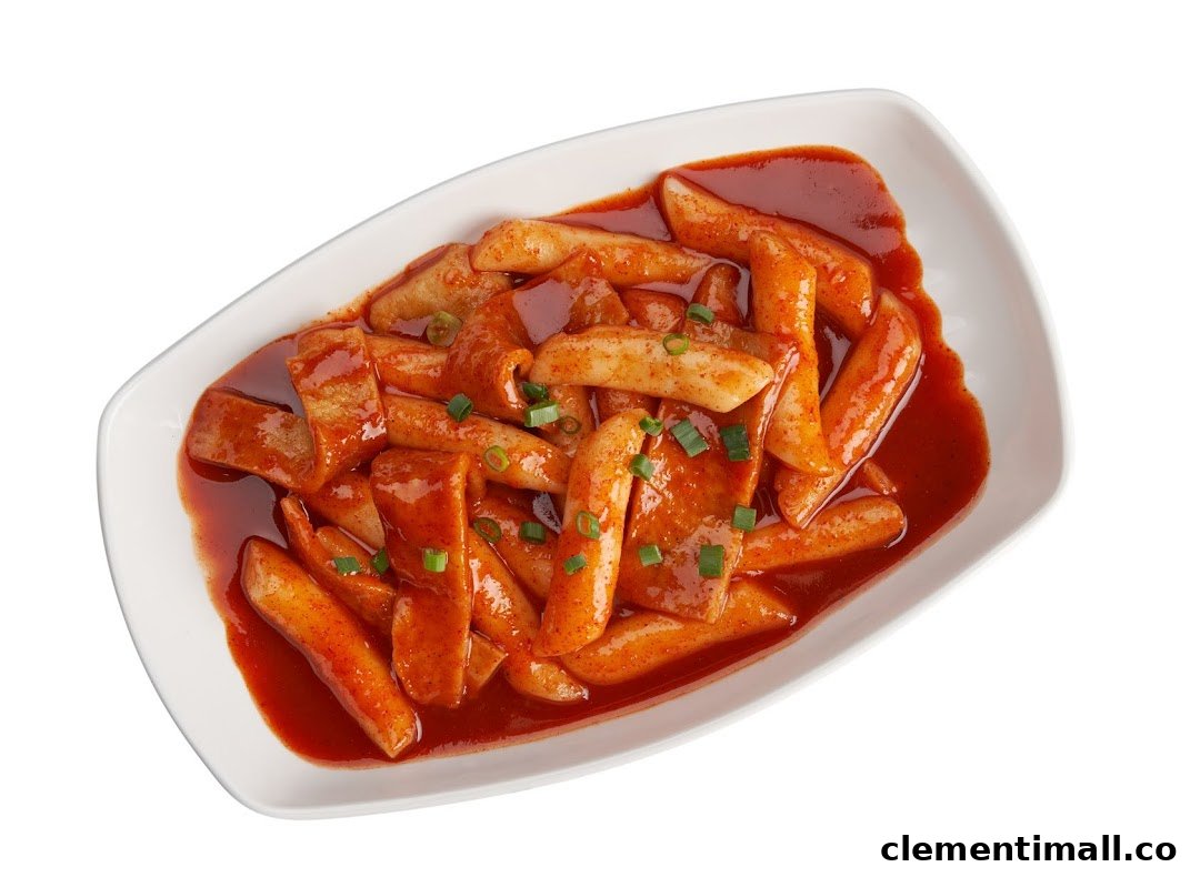 A white dish filled with spicy red Tteokbokki (Korean rice cakes) and fish cakes, garnished with green onions.