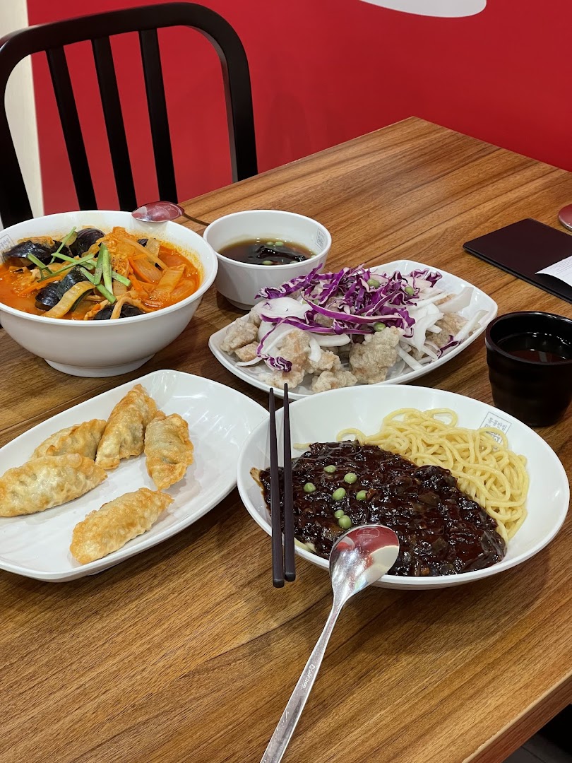 A table laden with various Korean dishes including Jajangmyeon, Jjamppong, fried dumplings, and sweet and sour chicken.