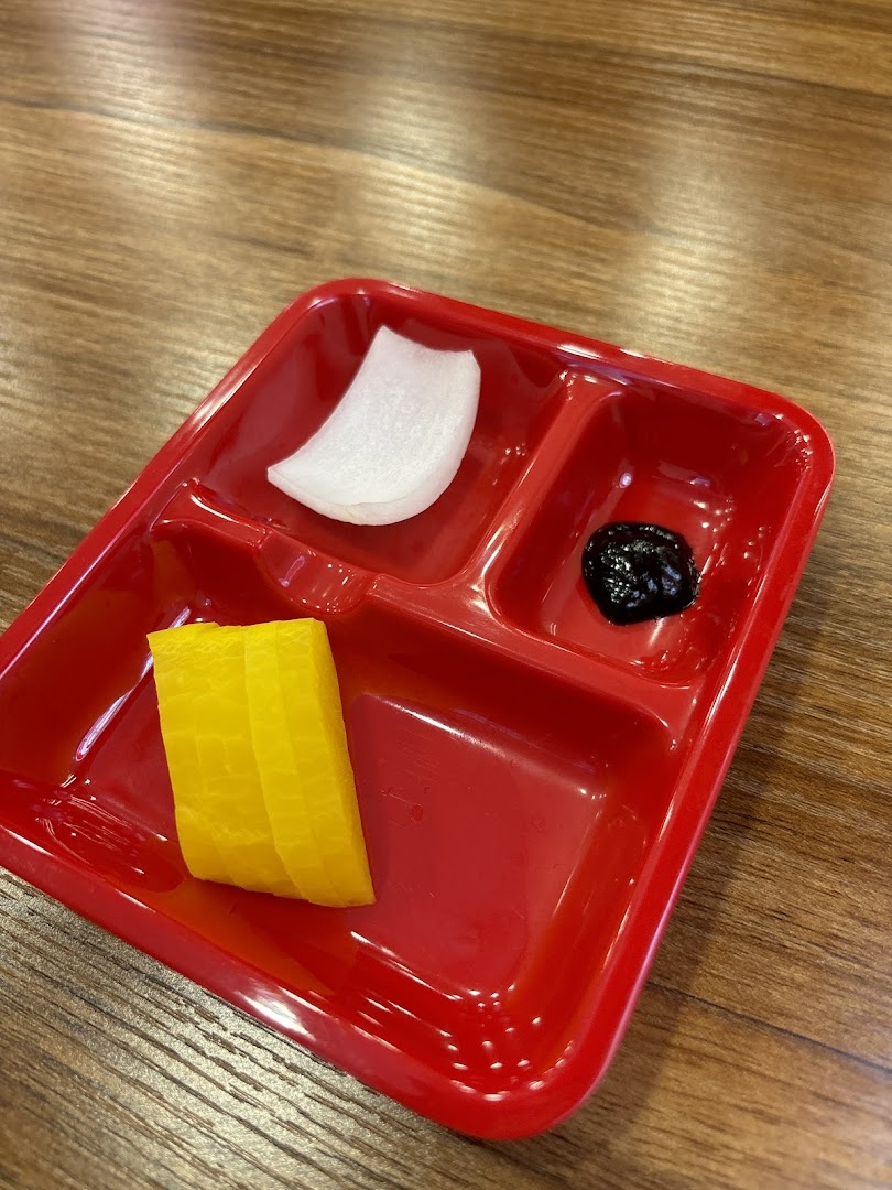 A red partitioned plate holds Korean side dishes: pickled radish and black bean paste.