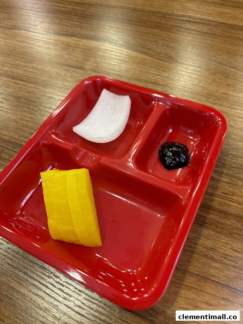 A red partitioned plate holds Korean side dishes: pickled radish and black bean paste.