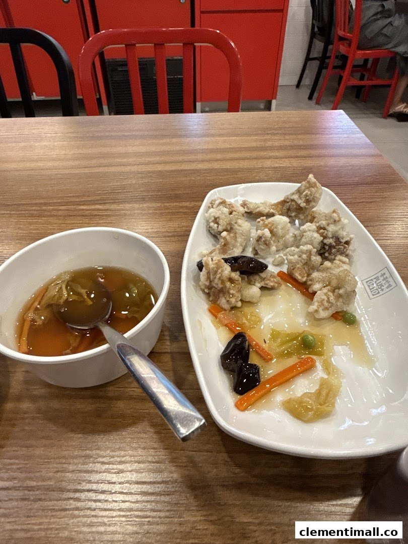 A close-up of a meal featuring fried chicken and a bowl of soup on a wooden table.