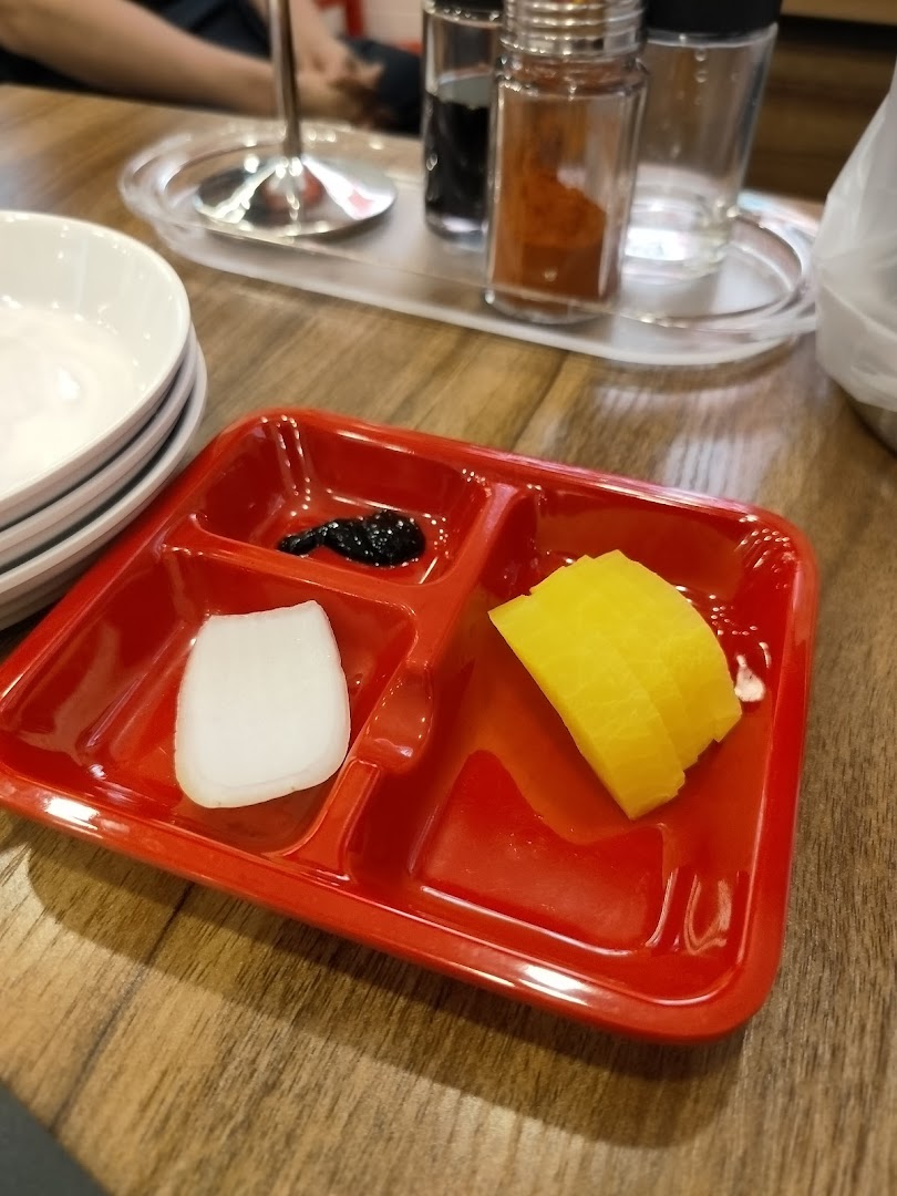 A red partitioned plate with Korean side dishes, including pickled radish and onion, on a wooden table.