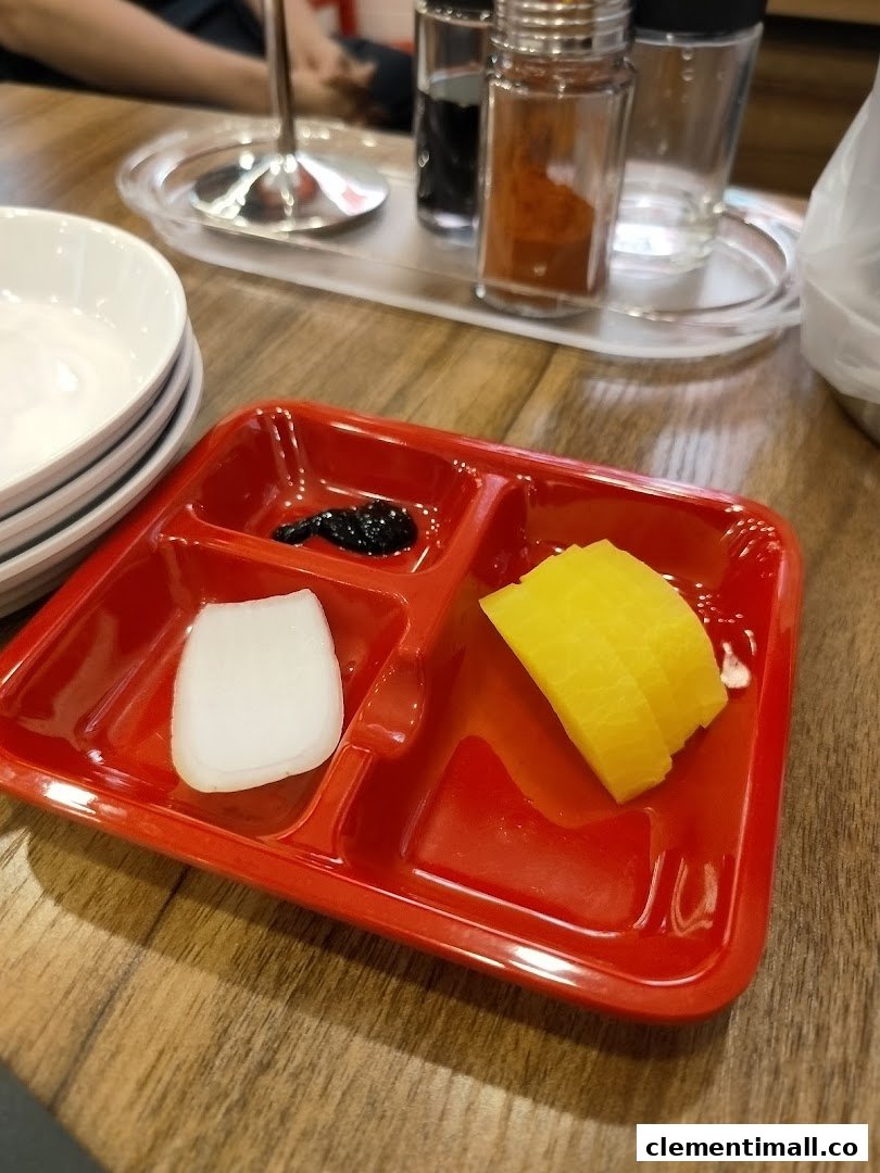 A red partitioned plate with Korean side dishes, including pickled radish and onion, on a wooden table.
