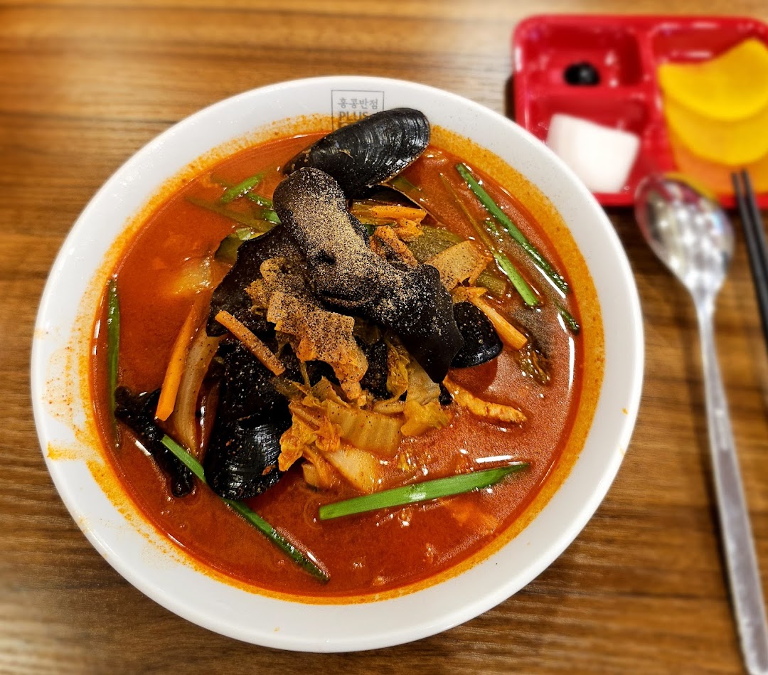 A vibrant bowl of spicy seafood noodles with mussels and vegetables, served with side dishes.