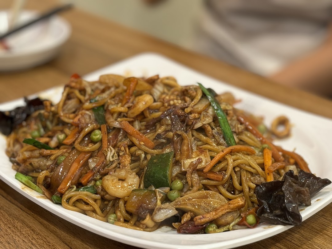 A close-up of a delicious plate of stir-fried noodles with shrimp, vegetables, and mushrooms.