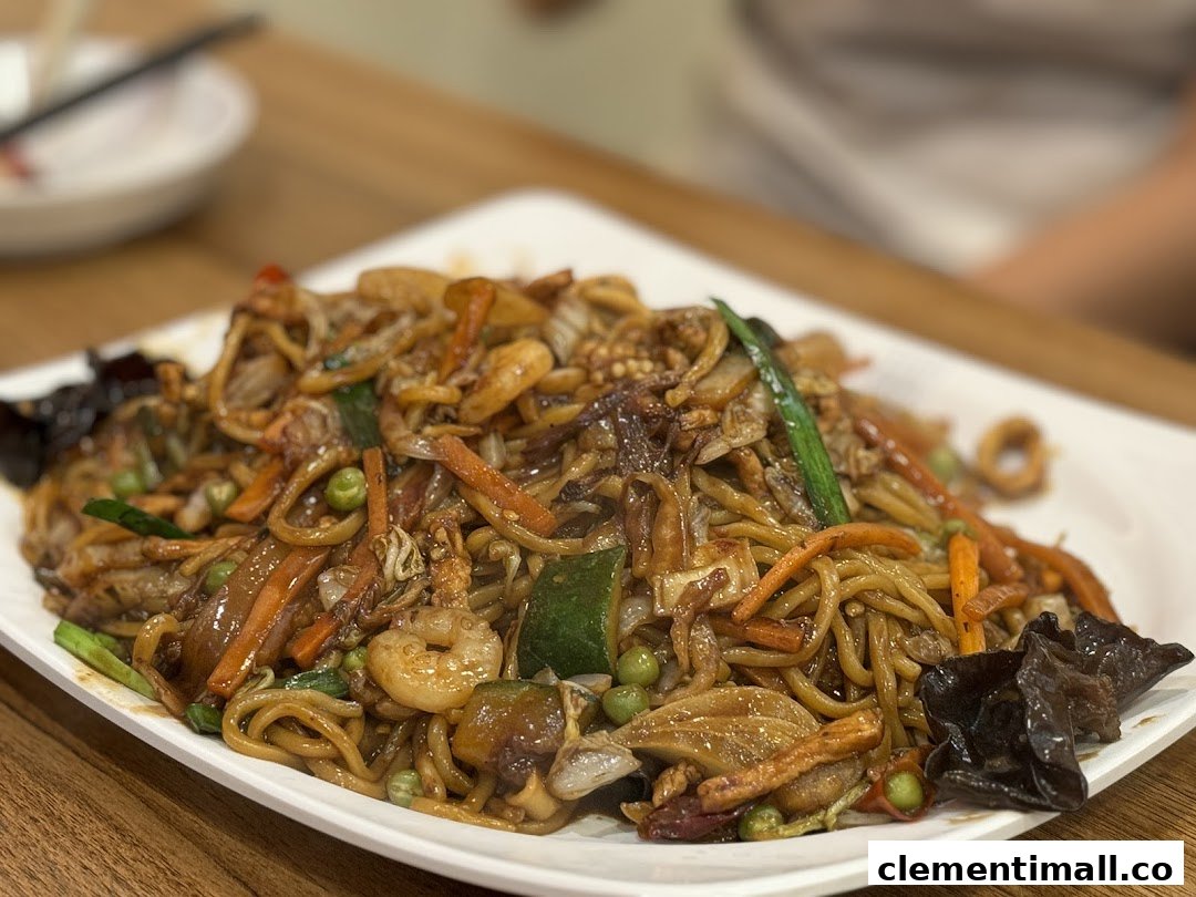 A close-up of a delicious plate of stir-fried noodles with shrimp, vegetables, and mushrooms.