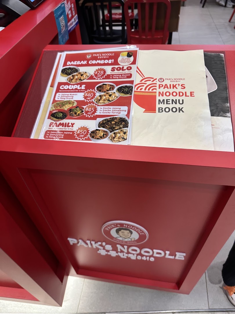 A red menu stand displaying Paik's Noodle 'Daebak Combos' and a menu book.