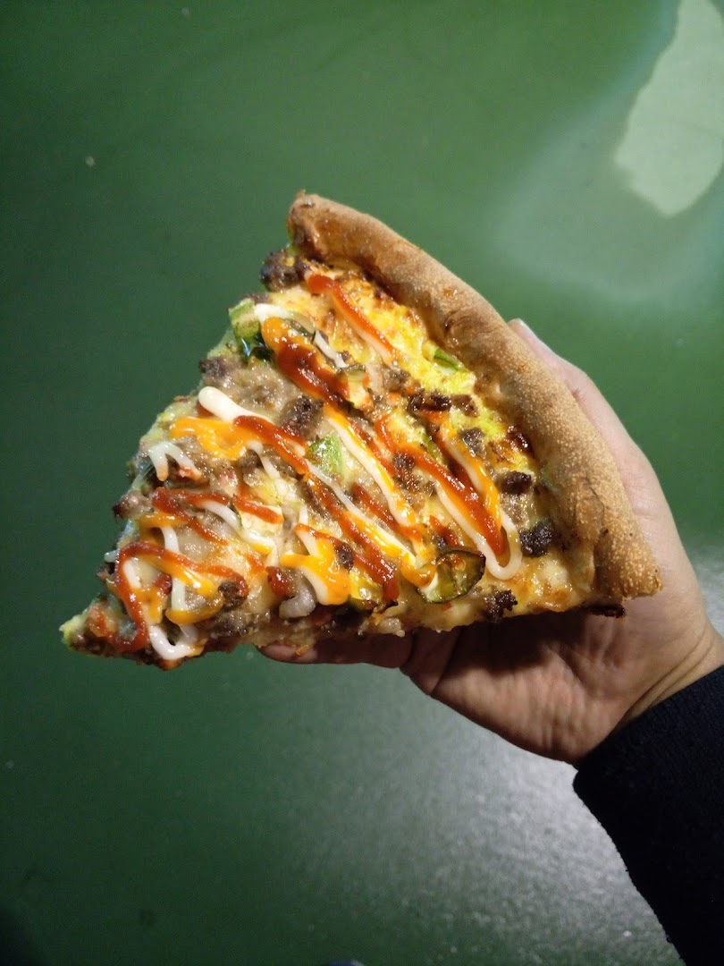 A hand holds a delicious slice of pizza topped with various sauces and ingredients.