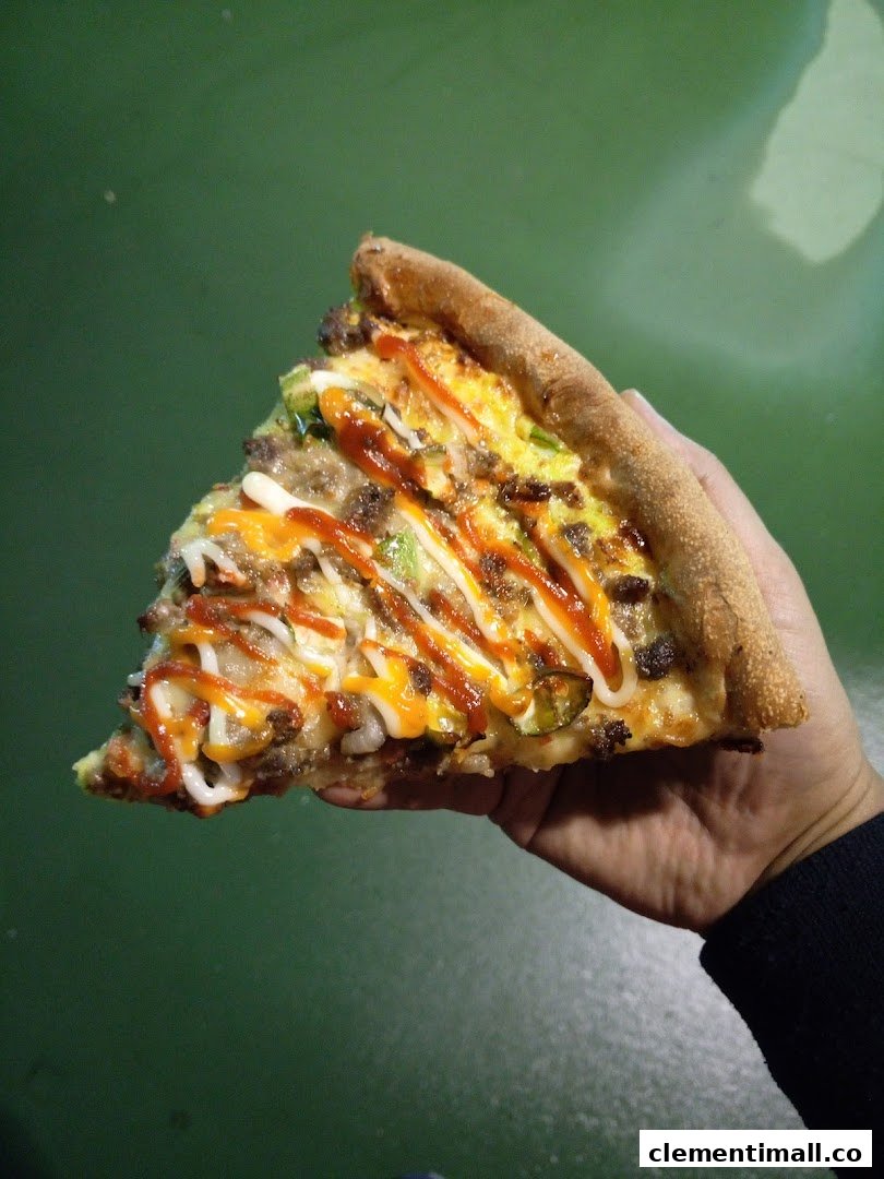 A hand holds a delicious slice of pizza topped with various sauces and ingredients.