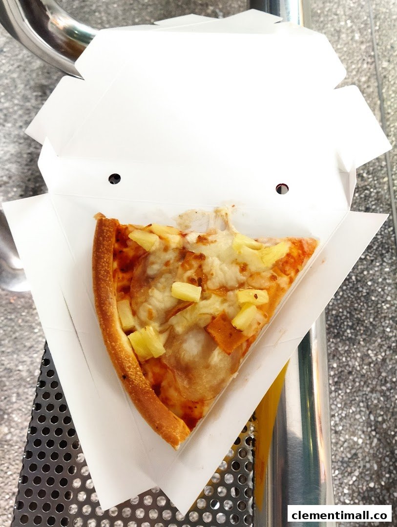 A delicious slice of Hawaiian pizza with pineapple and ham in a takeaway box.