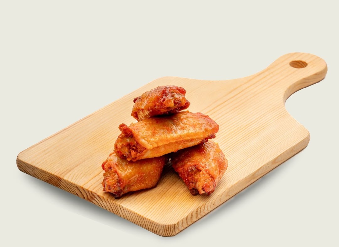 Four golden-brown chicken wings are stacked on a wooden cutting board.