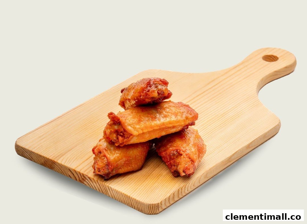 Four golden-brown chicken wings are stacked on a wooden cutting board.