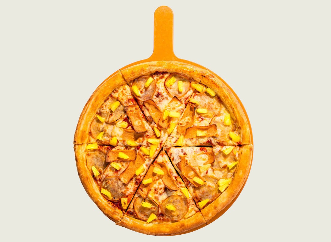 A whole pizza with pineapple and ham/bacon toppings, served on a wooden pizza peel.