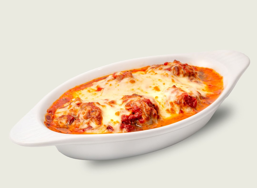 A white baking dish filled with cheesy meatballs in rich tomato sauce.
