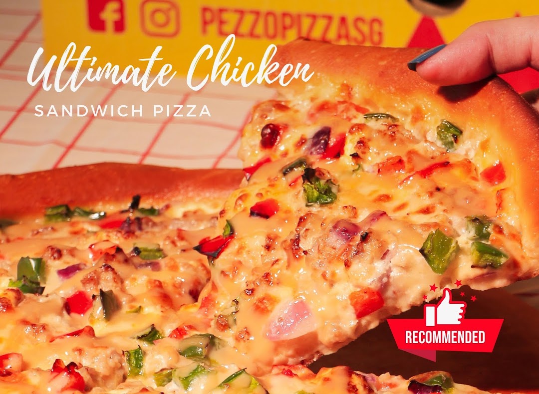 A hand holds a delicious slice of Pezzo's Ultimate Chicken Sandwich Pizza, showcasing melted cheese and vibrant toppings.