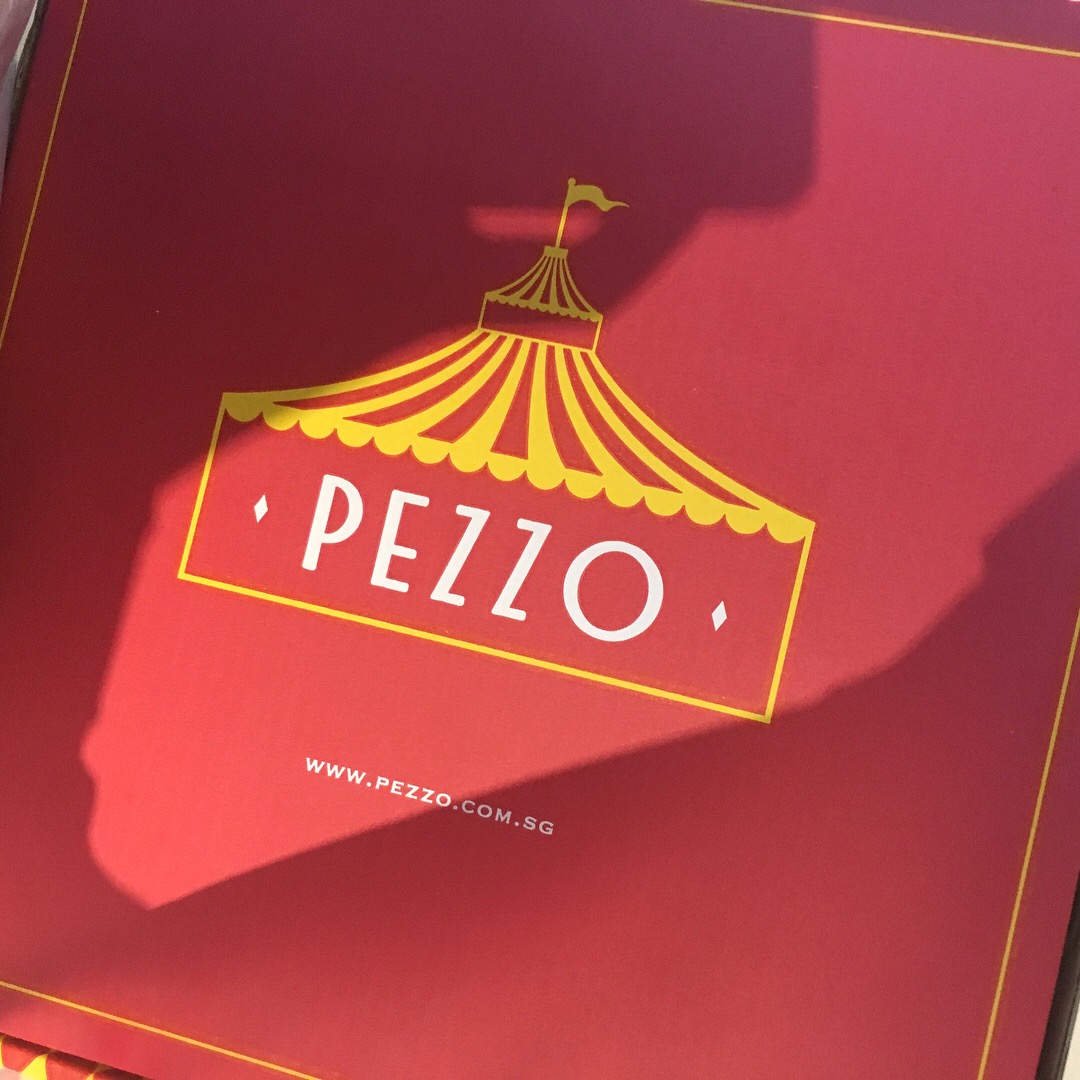 Close-up of a red Pezzo pizza box featuring the brand's distinctive circus tent logo and website.