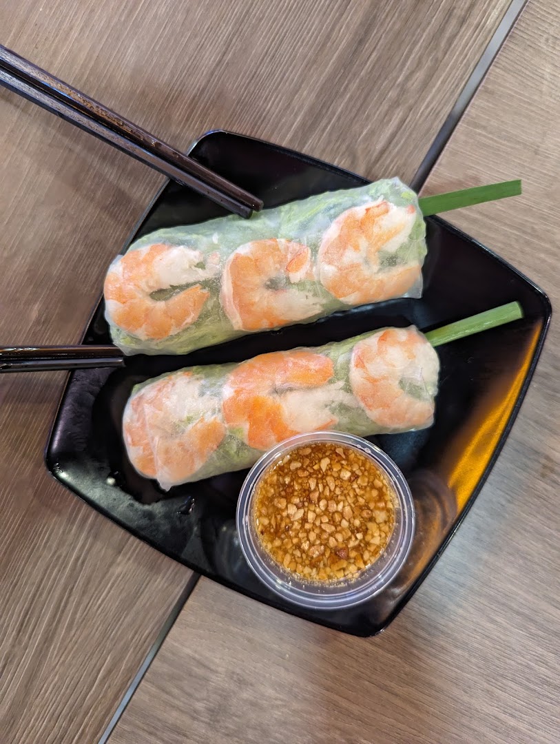 Two fresh Vietnamese spring rolls with shrimp and a peanut dipping sauce on a black plate.