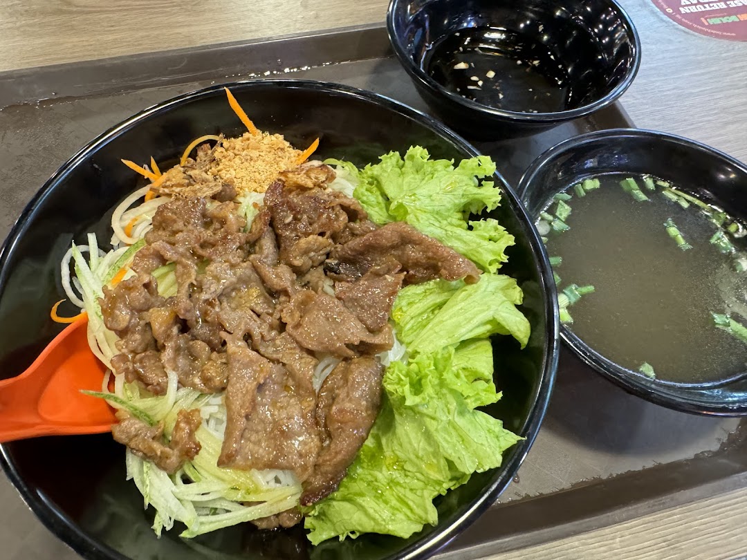 A delicious bowl of Vietnamese vermicelli noodles with grilled beef, fresh lettuce, and a side of clear soup.