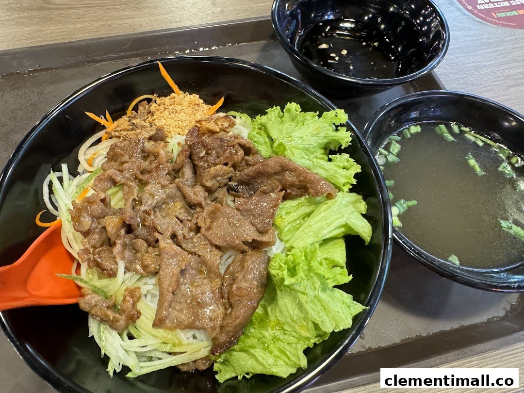 A delicious bowl of Vietnamese vermicelli noodles with grilled beef, fresh lettuce, and a side of clear soup.