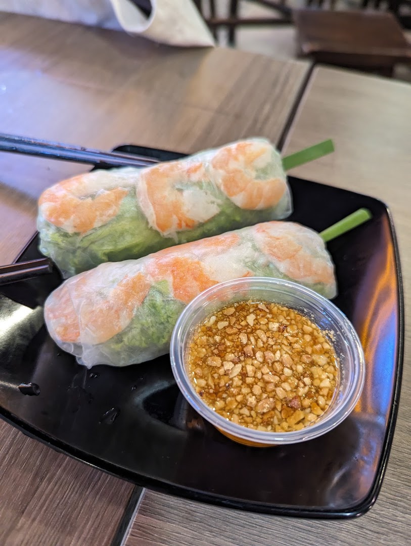 Two fresh Vietnamese spring rolls with shrimp and a peanut dipping sauce on a black plate.