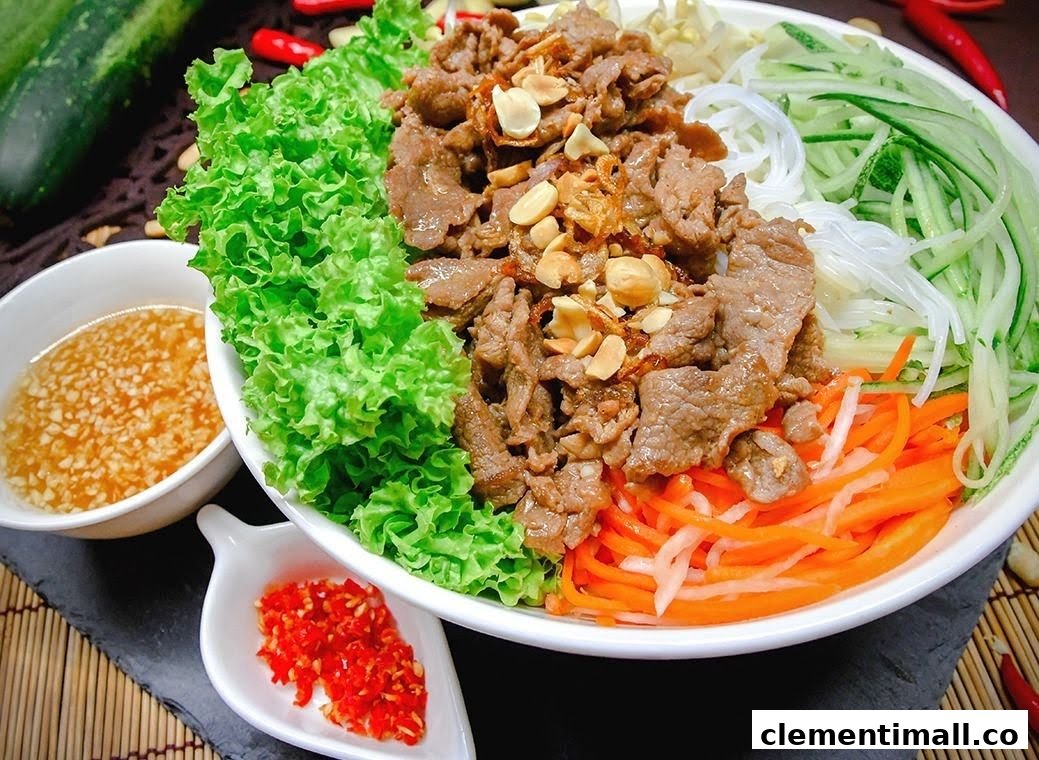 A vibrant bowl of Vietnamese beef noodle salad with fresh vegetables and a side of sauce.