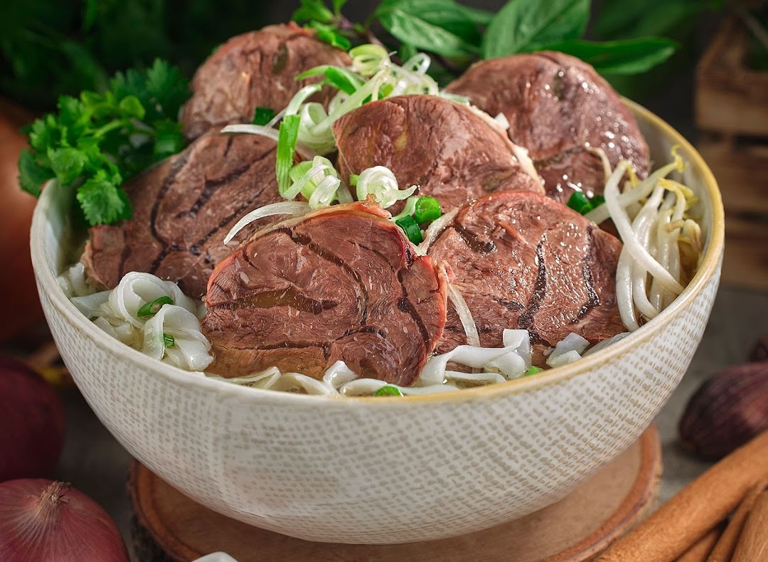 A close-up of a delicious bowl of Vietnamese pho with sliced beef, noodles, and fresh herbs.
