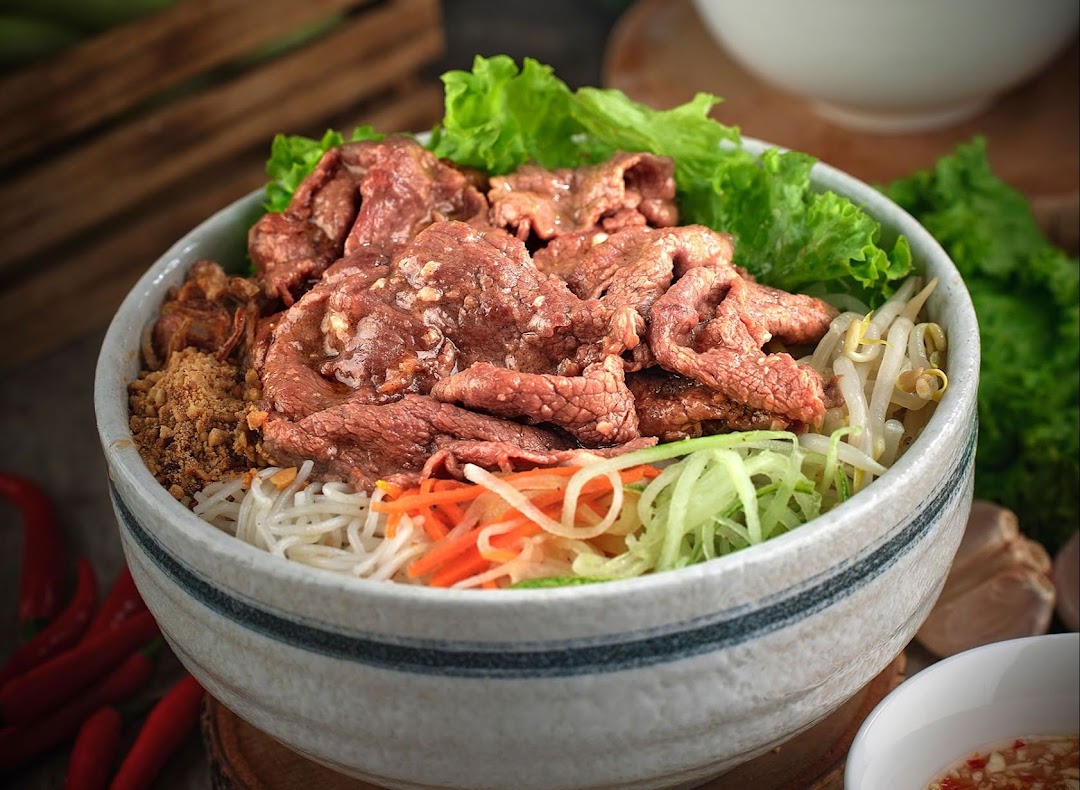 A close-up of a vibrant Vietnamese noodle bowl featuring beef, fresh vegetables, and peanuts.
