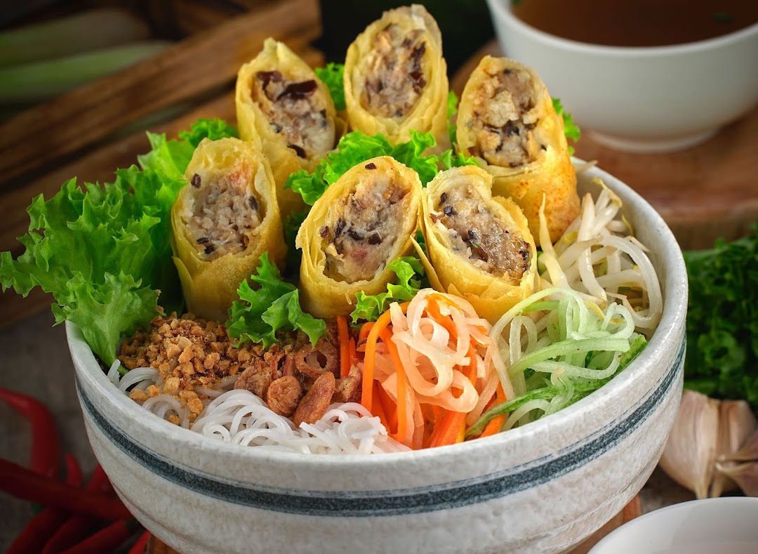 A vibrant bowl of Vietnamese vermicelli noodles with crispy spring rolls and fresh vegetables.