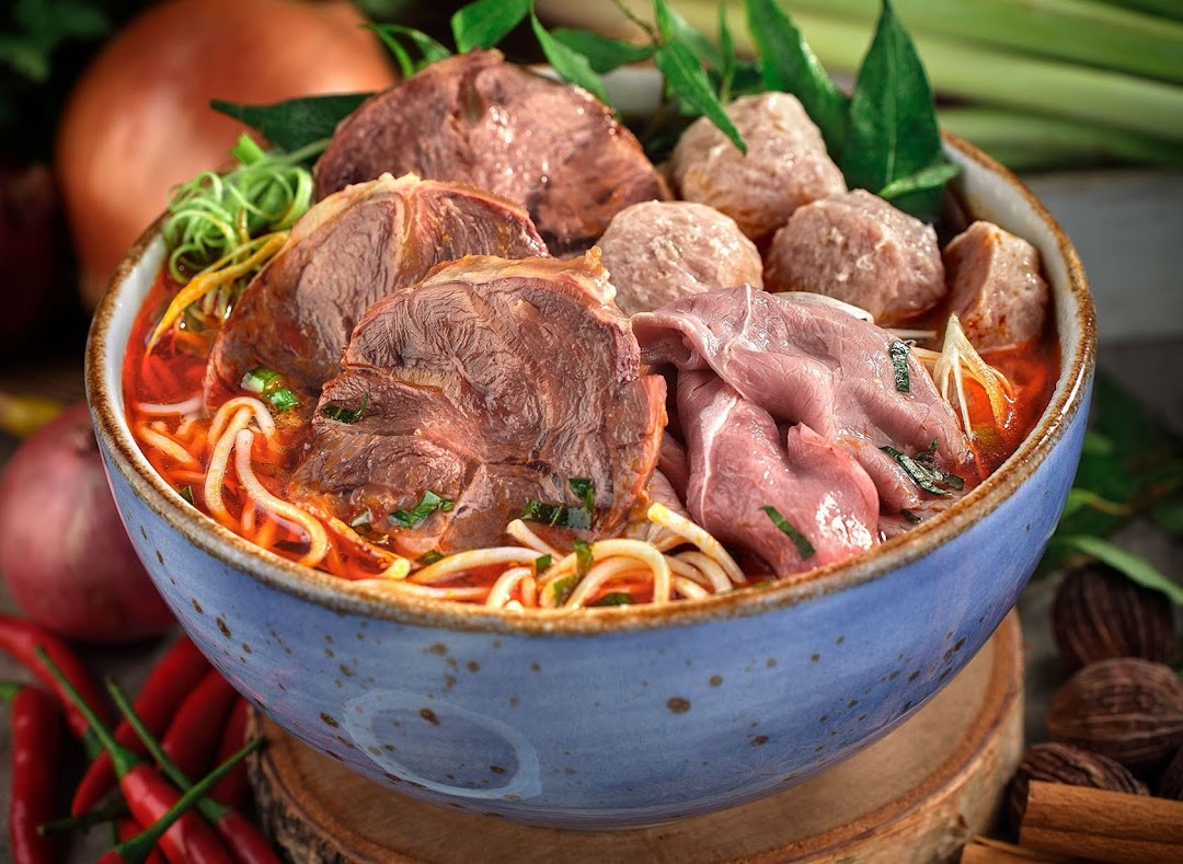 A vibrant bowl of Vietnamese pho with various cuts of beef, meatballs, noodles, and fresh herbs.