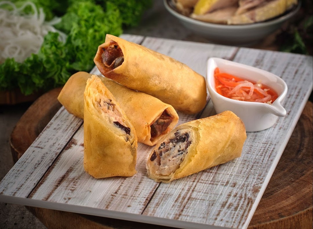 Crispy Vietnamese fried spring rolls served with a tangy dipping sauce on a rustic wooden board.
