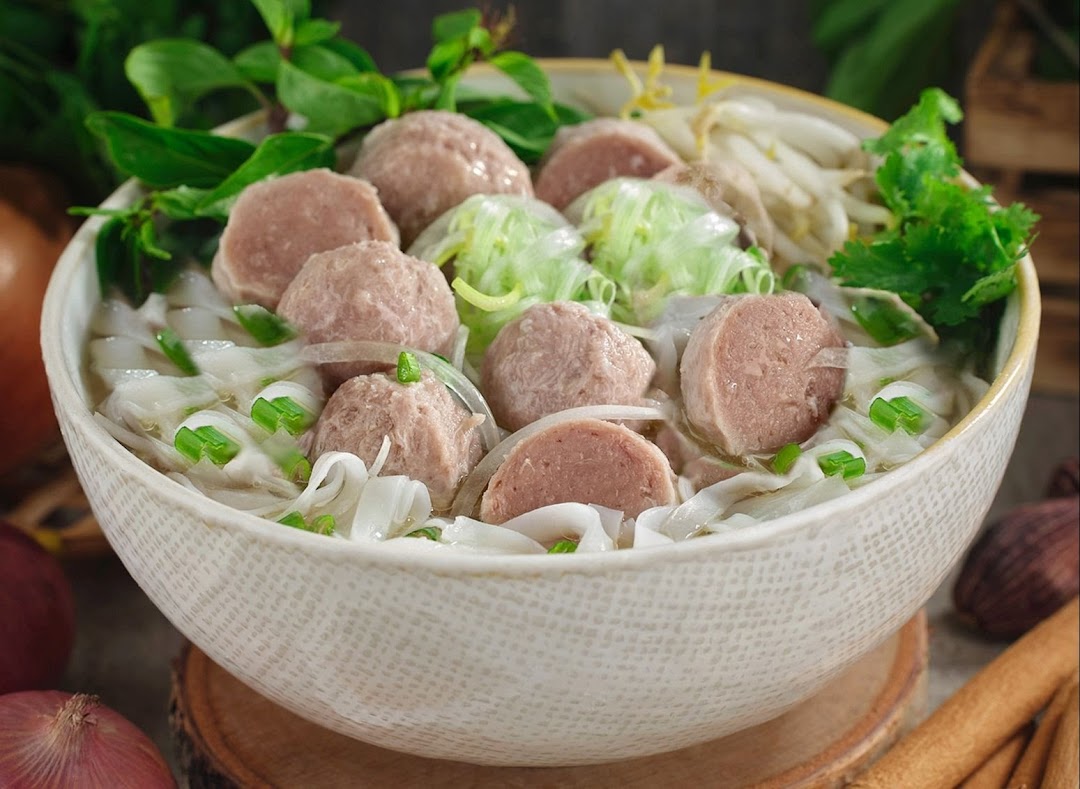 A close-up of a delicious bowl of Vietnamese pho with meatballs, rice noodles, and fresh herbs.