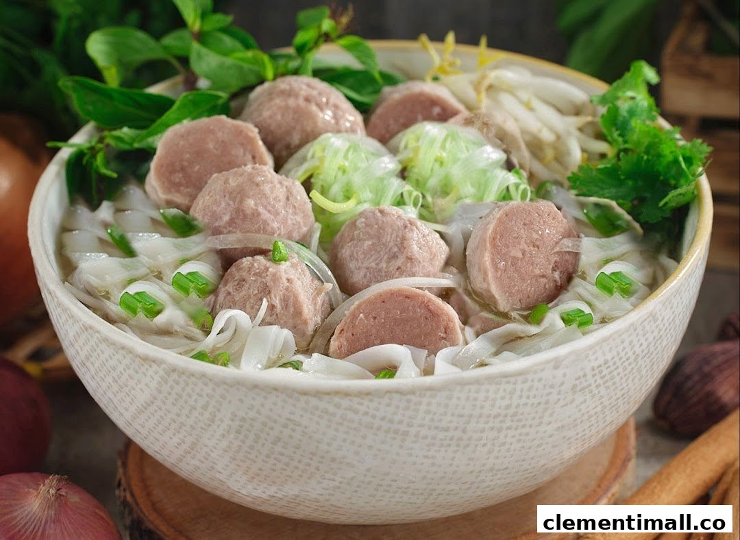 A close-up of a delicious bowl of Vietnamese pho with meatballs, rice noodles, and fresh herbs.