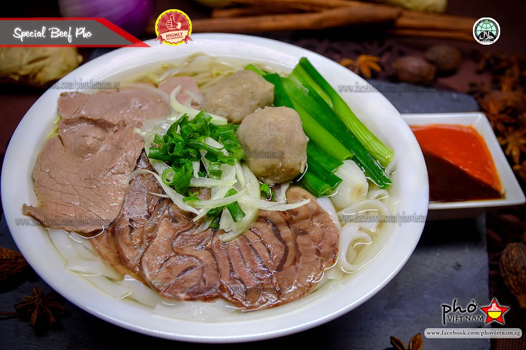 A close-up of a Special Beef Pho bowl with beef slices, meatballs, and fresh herbs.