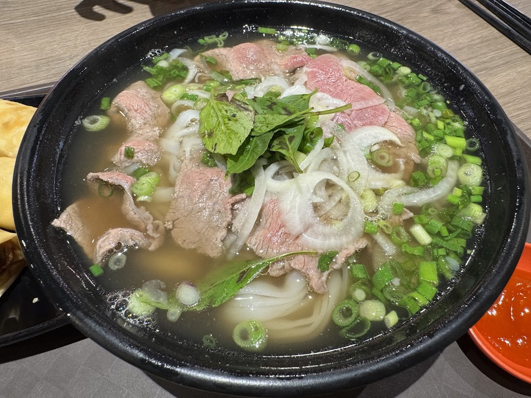 A close-up of a delicious bowl of Vietnamese pho with beef, noodles, and fresh herbs.