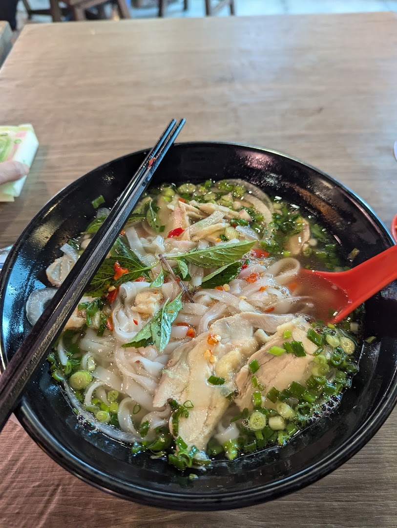 A close-up of a delicious bowl of chicken pho with fresh herbs and noodles.