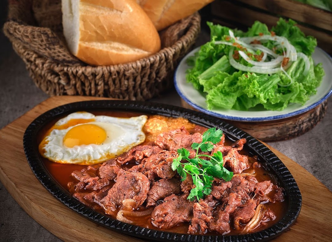 A sizzling plate of Vietnamese beef with fried eggs, served with fresh bread and salad.