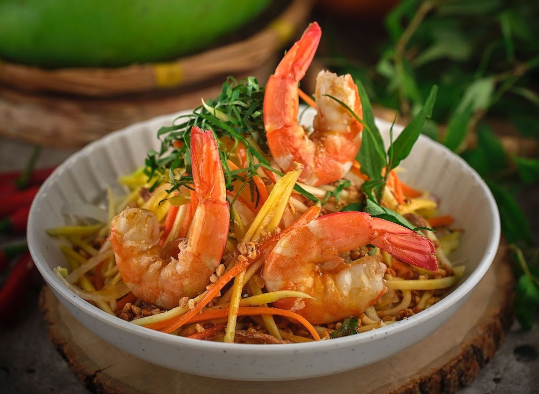 A vibrant Vietnamese salad featuring fresh shrimp, shredded mango, and herbs in a white bowl.
