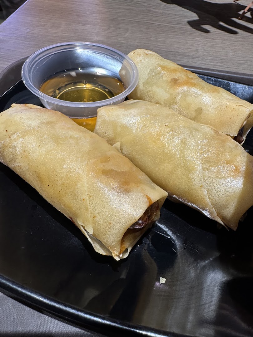 Three golden fried spring rolls served with a dipping sauce on a black plate.