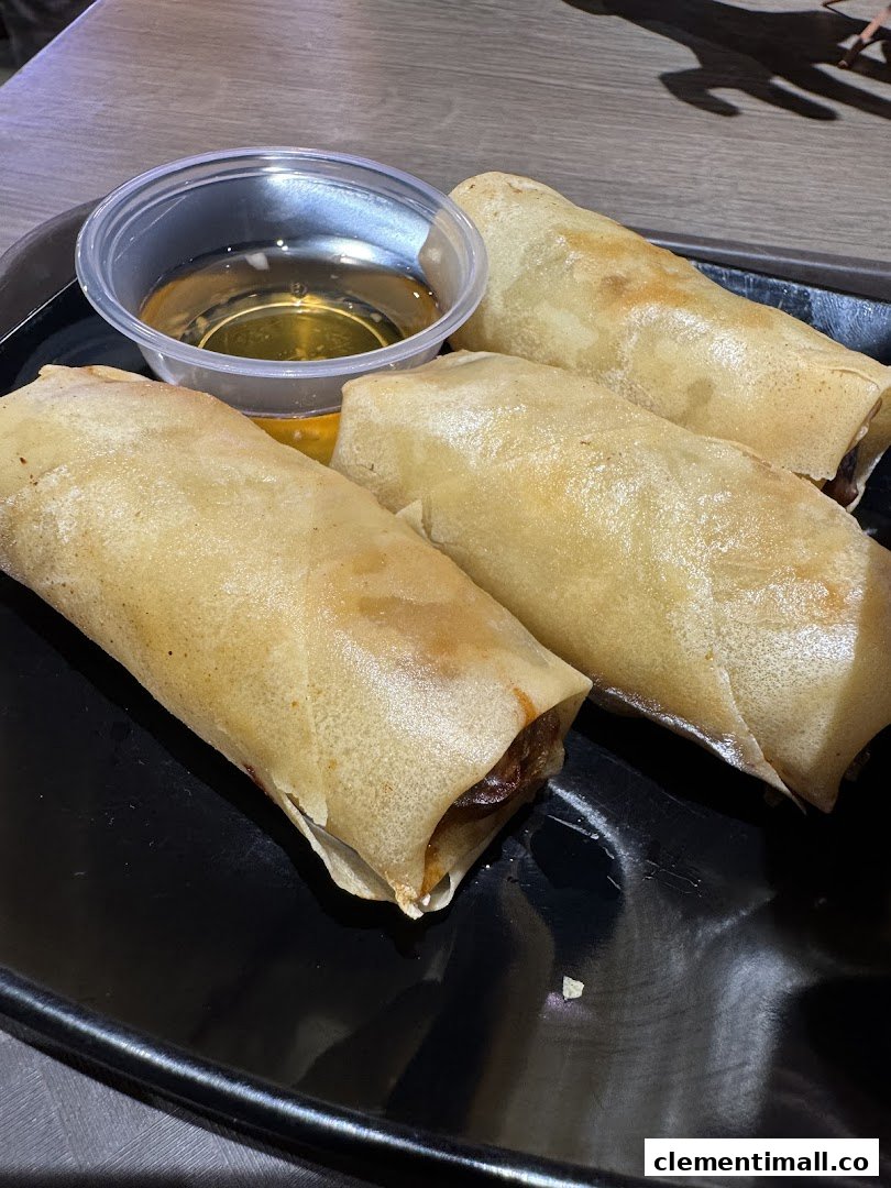 Three golden fried spring rolls served with a dipping sauce on a black plate.