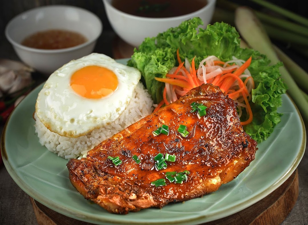 A vibrant Vietnamese dish featuring grilled chicken, rice, fried egg, and fresh vegetables.