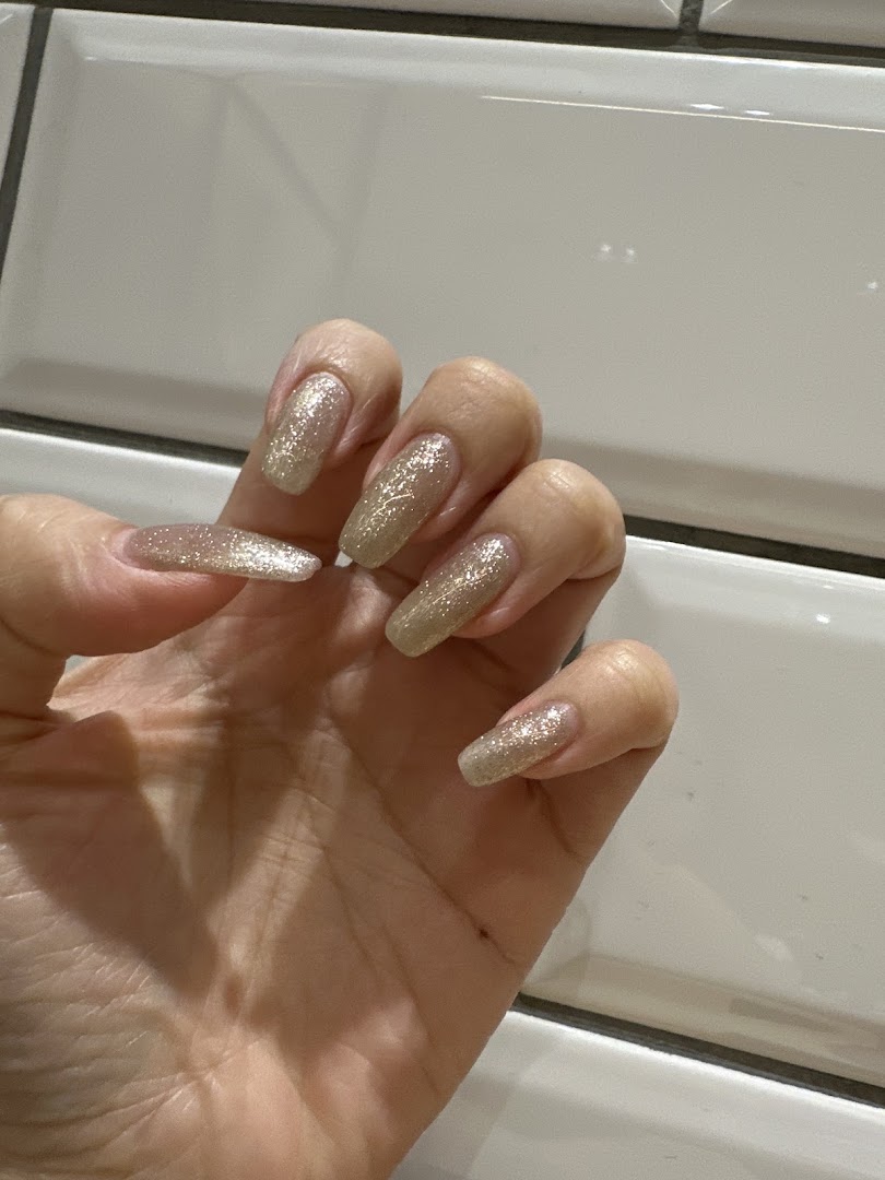 A hand showcasing long, coffin-shaped nails with sparkling gold glitter polish.