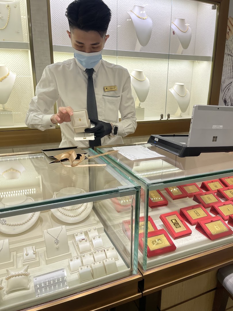 A masked staff member at Poh Heng Jewellery presents a gold item in a display-filled store.